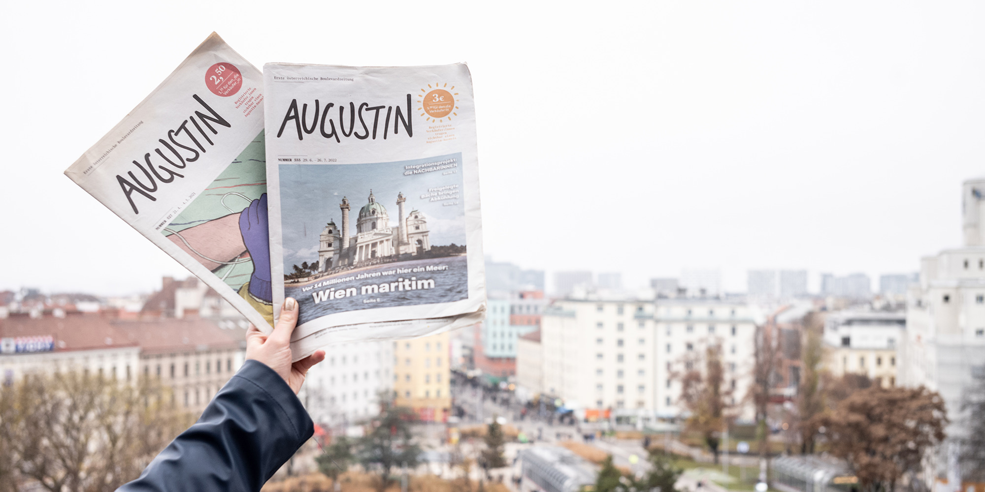 Redakteurin hält zwei Augustinausgaben, im Hintergrund der Wiener Reumannplatz